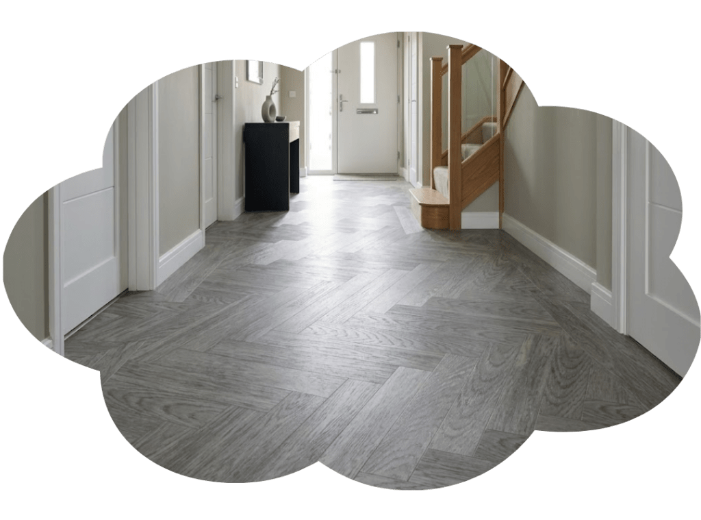 Modern hallway with gray herringbone wood flooring, white walls, and wooden staircase leading upstairs.