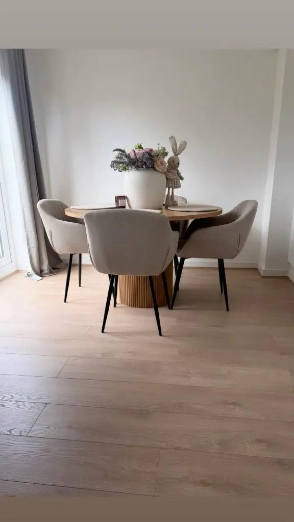 Modern round dining table with two gray upholstered chairs, white vase with flowers, and decorative bunny figurine