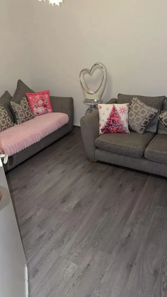 Cozy living room with two gray sofas, pink throw pillows, Christmas decorations, and a silver heart-shaped lamp on dark wood flooring.