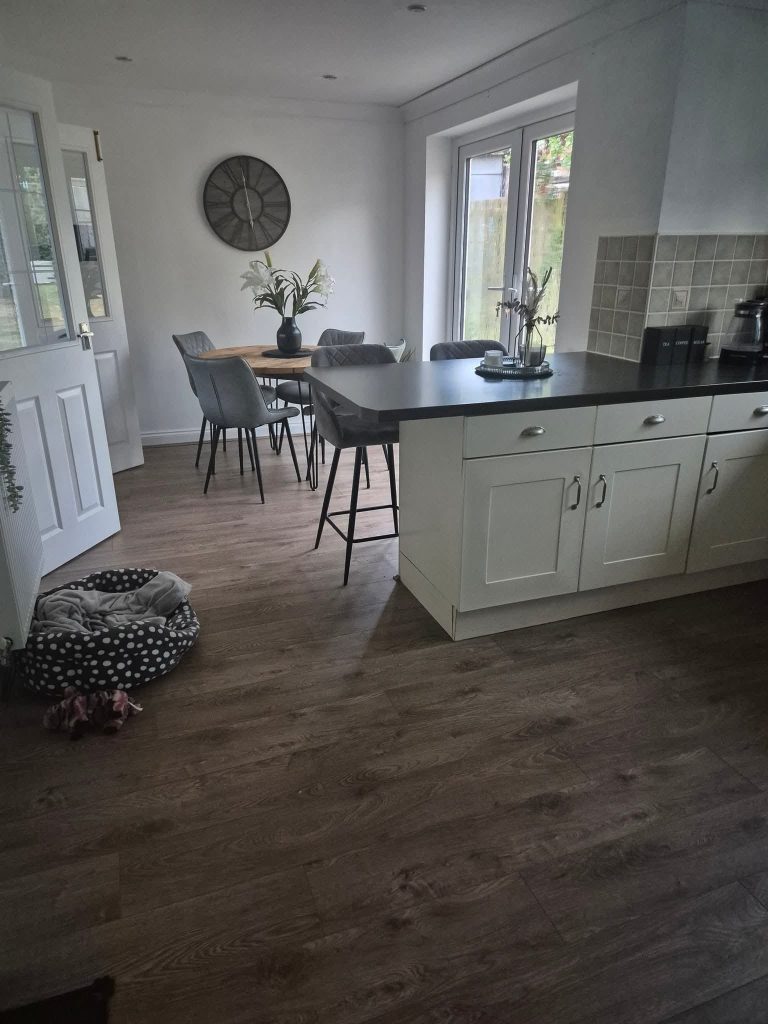 Modern open-plan kitchen and dining area with cream cabinetry, black countertop island, dining table, and wooden flooring