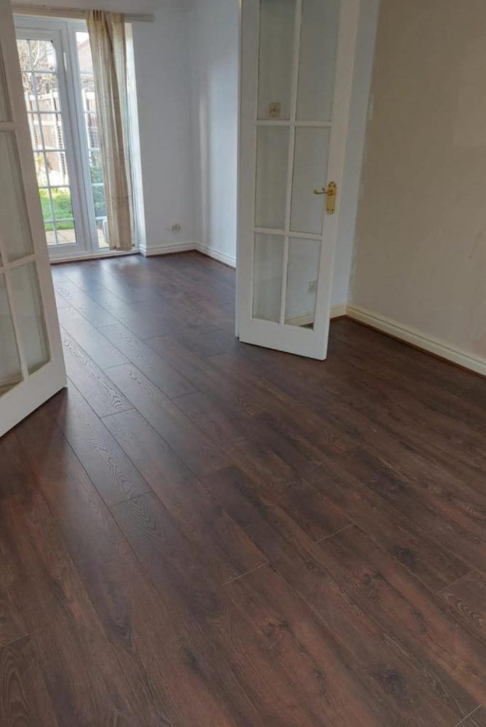 Empty modern living room with dark wood flooring, white walls, glass doors, and garden view through patio doors
