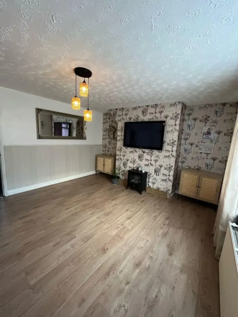 Modern living room with wood flooring, patterned wallpaper, wall-mounted TV, pendant lights, and fireplace stove.