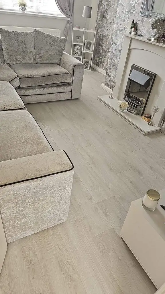 Modern gray living room with crushed velvet sofa, wood-effect flooring, fireplace, and elegant neutral décor.