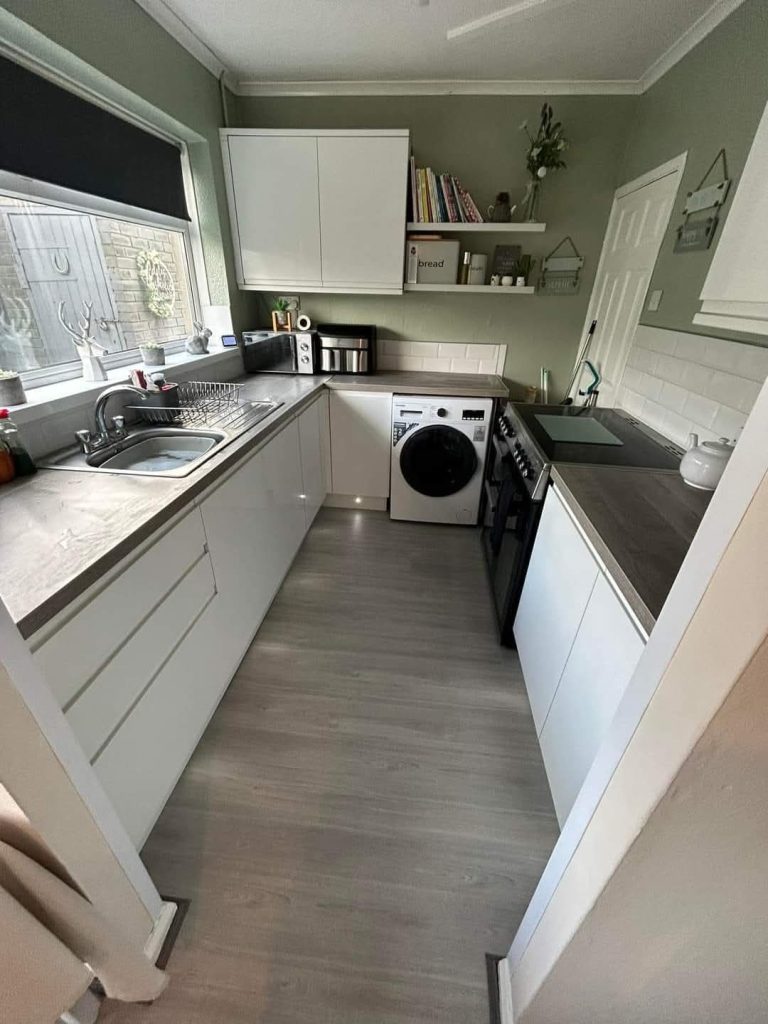 Modern kitchen with white cabinets, sage green walls, stainless steel appliances, and dark wood flooring
