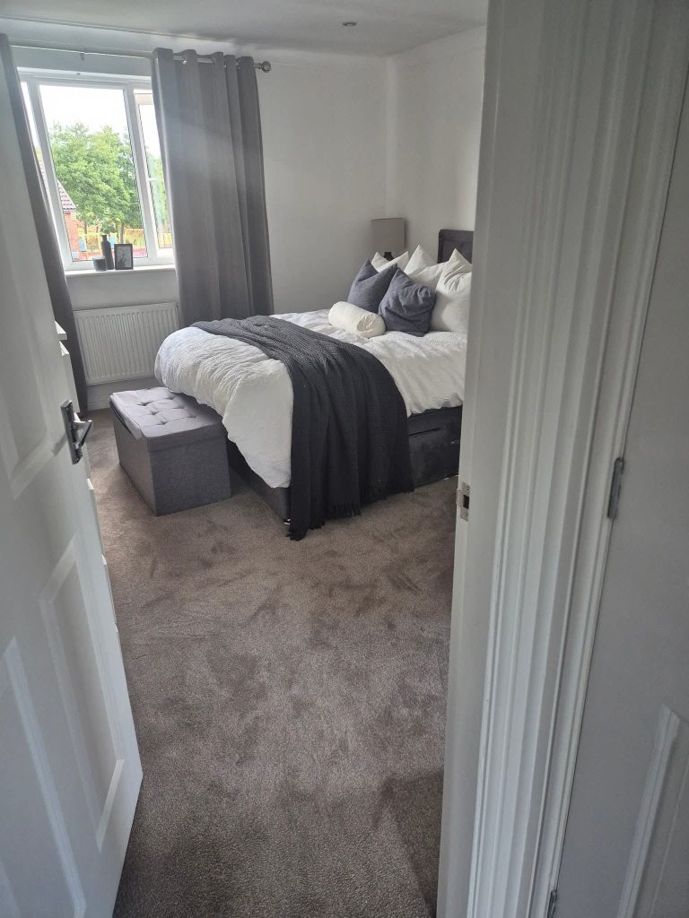 Modern bedroom with double bed, gray bedding, dark headboard, window with curtains, and neutral décor