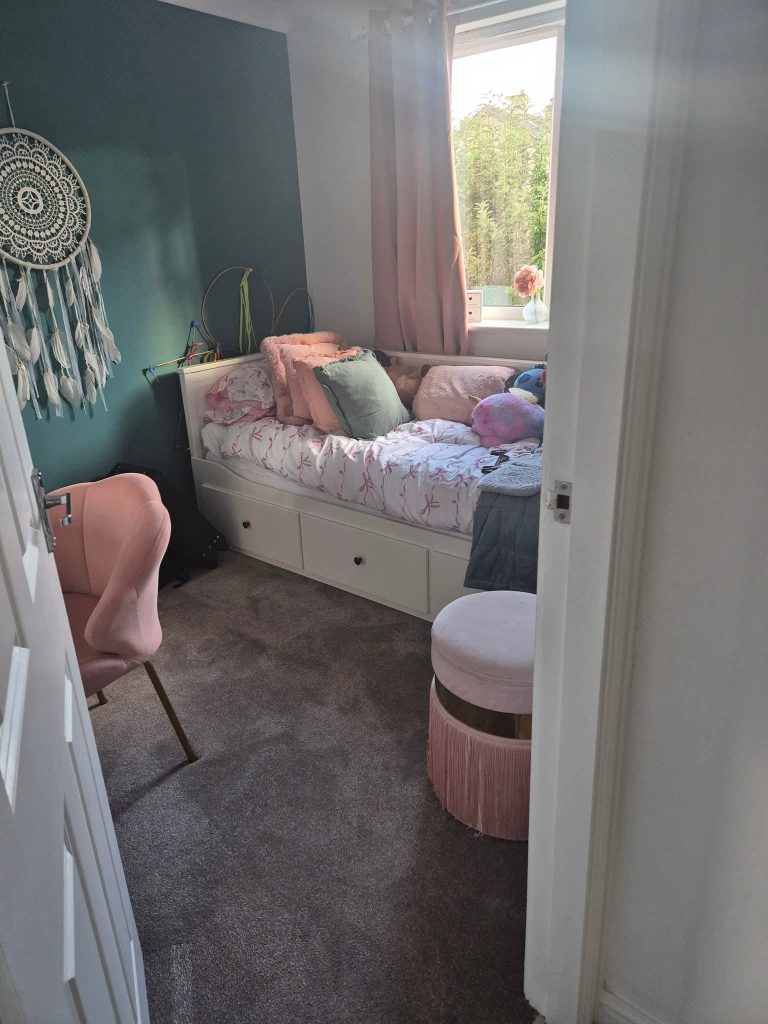 Cozy teenage girl's bedroom with teal accent wall, white bed with pink bedding, pink chair, and dreamcatcher decoration.