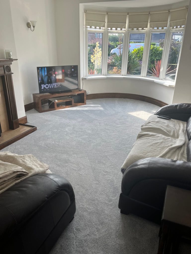 Spacious living room with curved bay windows, black leather sofas, wooden TV stand, and garden views during daytime.