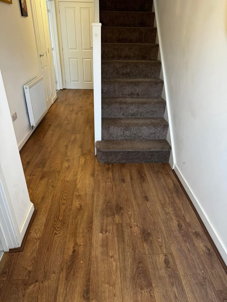 Modern hallway with dark brown carpet stairs and wooden laminate flooring, white walls and closed doors.