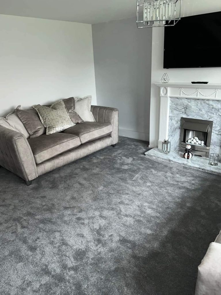 Modern living room with beige sofa, gray carpet, white marble fireplace, and wall-mounted TV