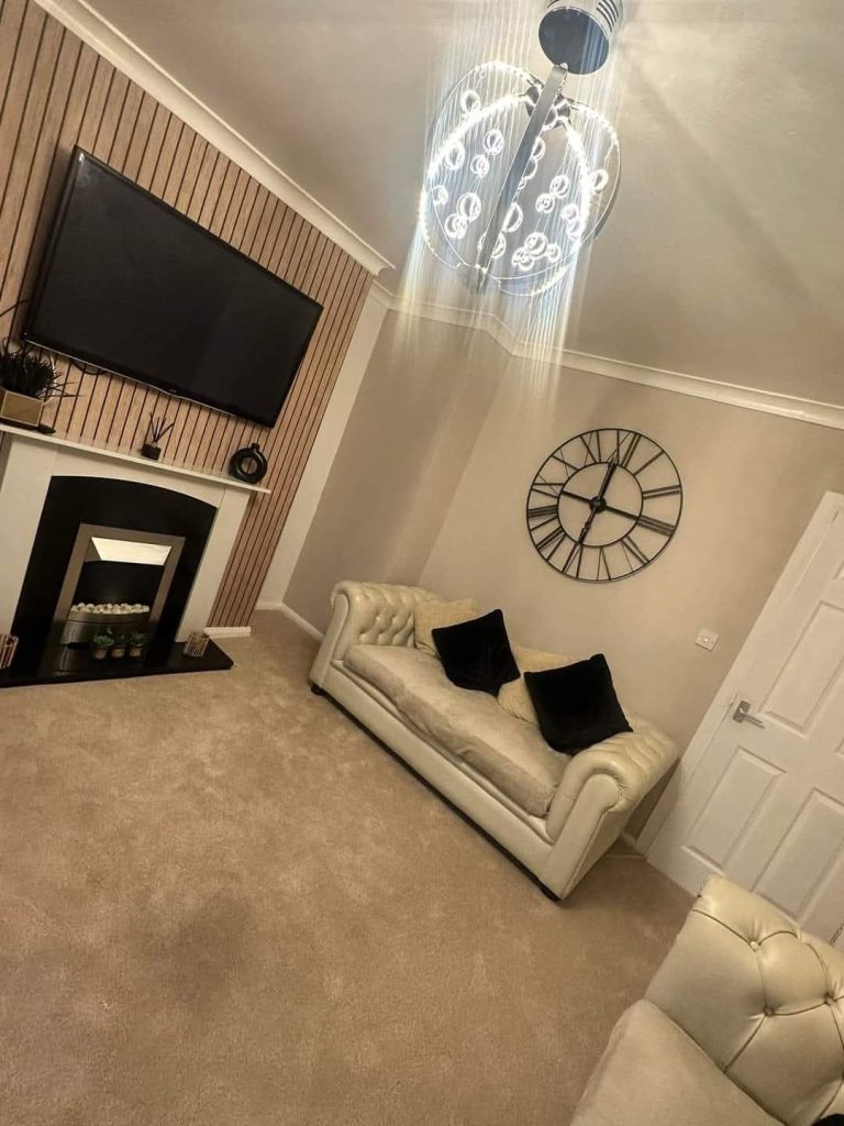 Modern living room with cream sofa, fireplace, TV, decorative clock, and pendant light fixture