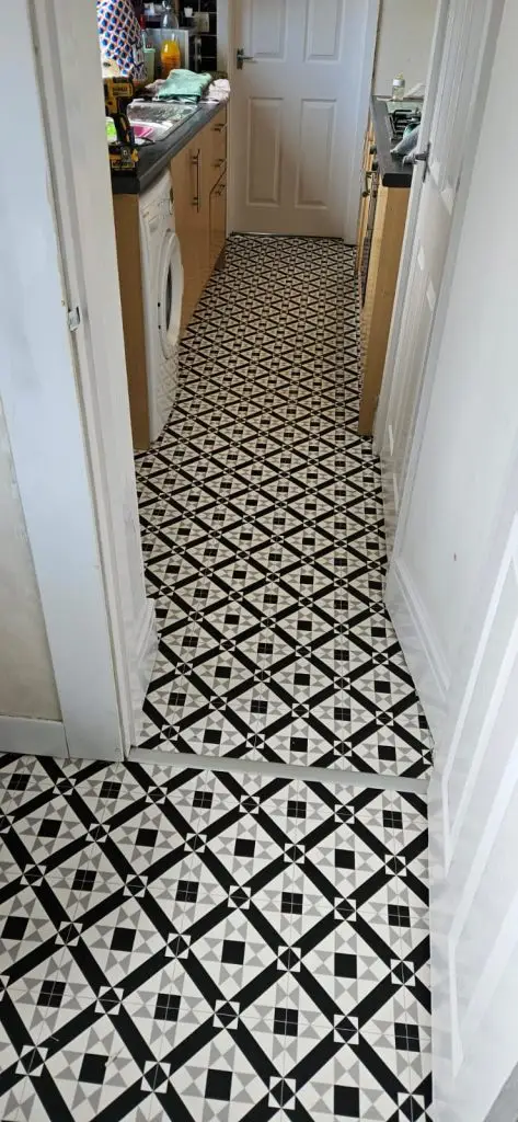 Narrow laundry room with black and white geometric tile flooring, washer and dryer units on sides, and storage cabinets.