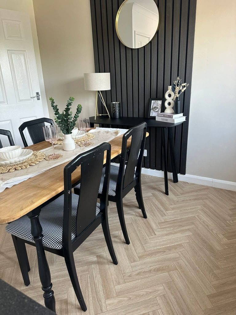 Modern dining room with wooden table, black chairs, and dark striped accent wall with gold mirror and decorative accessories.