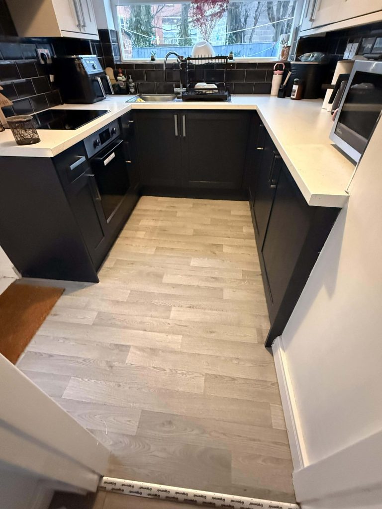 Modern black and white kitchen with U-shaped layout, white countertops, and wood-look flooring with large window view.