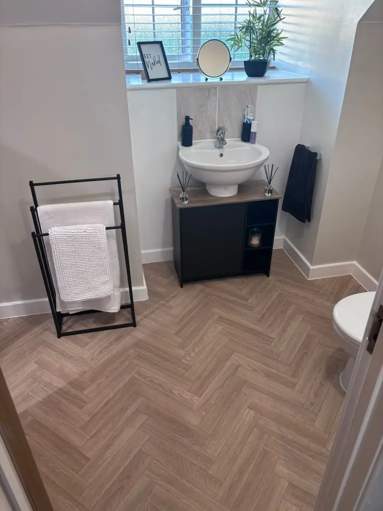 Modern bathroom with herringbone wood flooring, pedestal sink, black vanity, and towel rack