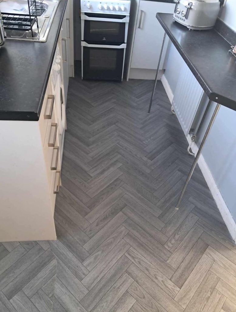 Modern kitchen with herringbone gray wood-effect flooring, white cabinets, and stainless steel appliances including double oven.