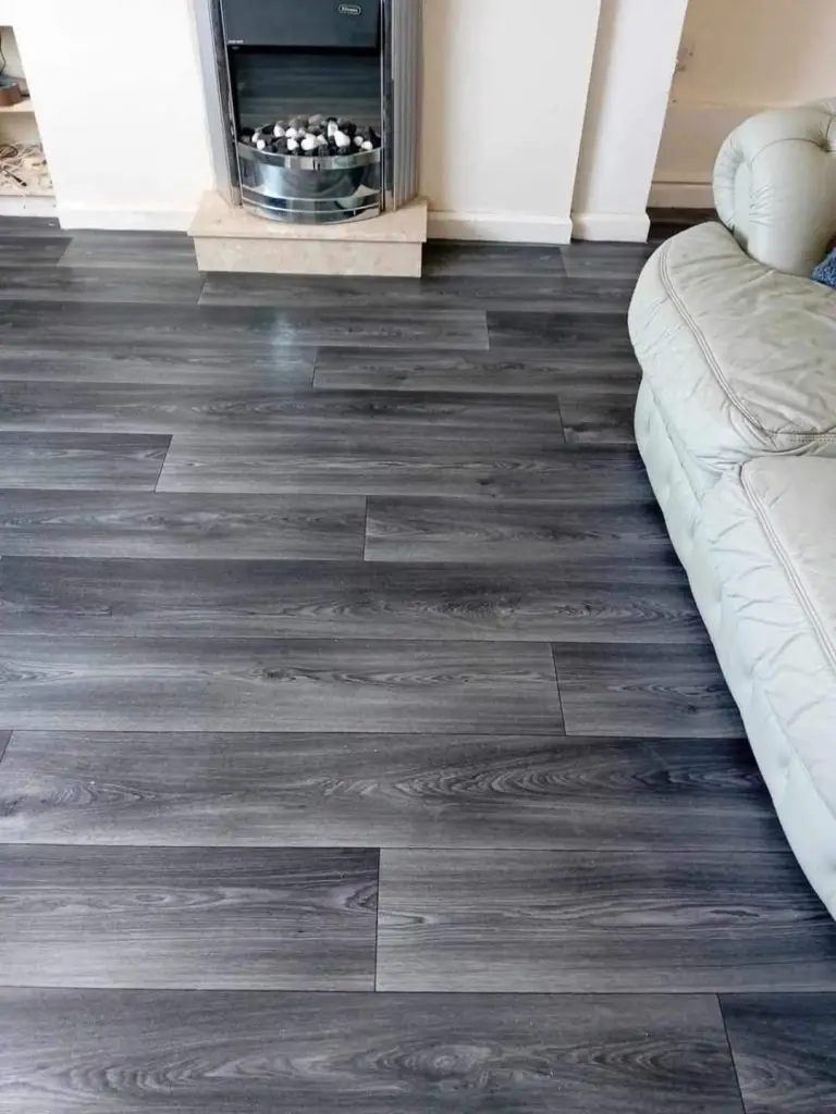Modern living room with dark gray laminate flooring, cream sofa, and fireplace with white mantel and black insert.