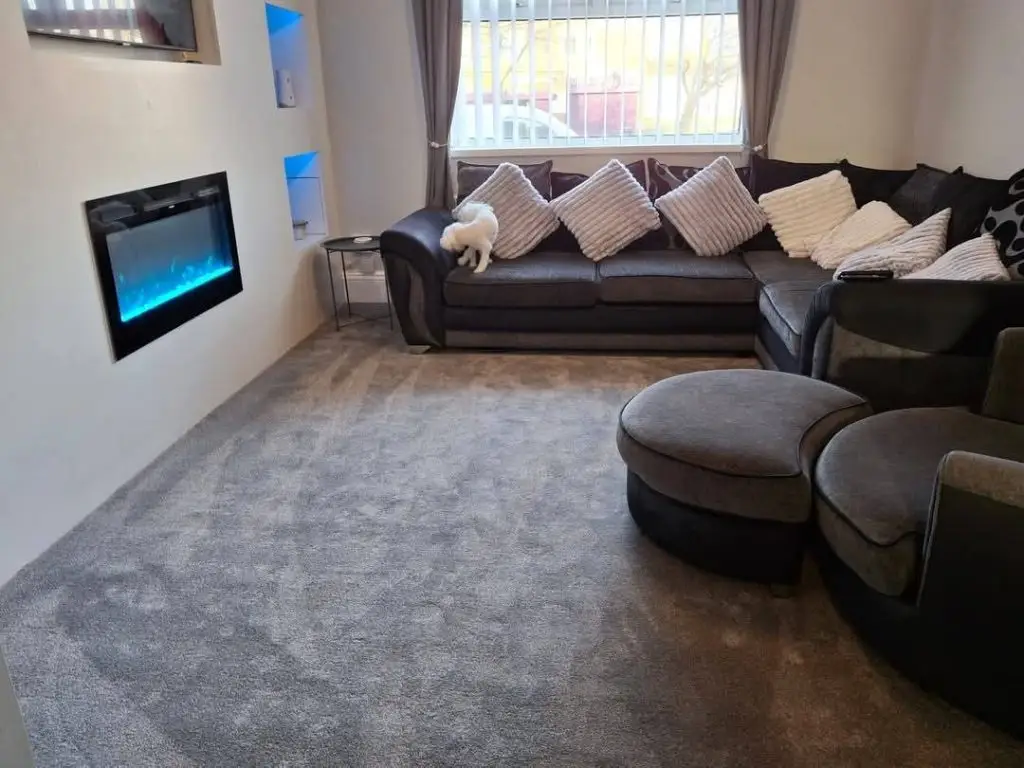 Modern living room with black sectional sofa, decorative pillows, electric fireplace, and gray carpet flooring.