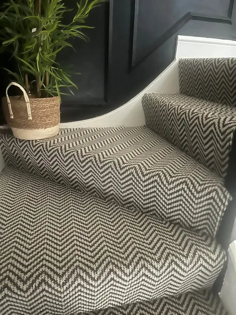 Modern entryway with herringbone patterned carpet, white bench seating, and potted plant in woven basket.